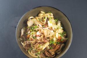 Seafood Udon Noodles topped with crispy tempura flakes and green onions including shrimp, squid, and fish cakes served in bowl isolated black background top view of Japanese comfort food photo