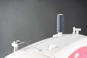 Spool of gray sewing thread stands on top of a white modern sewing machine photo
