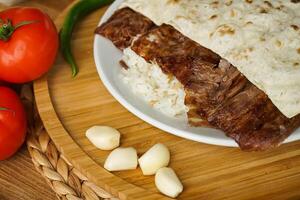 Meat Doner Kebab on Rice portion and Pita Bread served in plate with garlic, tomato, and green chilli isolate on wooden board closeup side view of arabic and turkish fast food photo