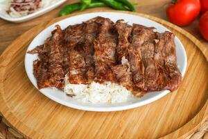 Meat Doner Kebab on Rice portion served in tray dish with garlic, tomato, and green chilli isolate on wooden board top view of arabic and turkish fast food photo