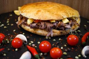 Meat Tombik Doner Kebab Sandwich with tomato, garlic, red pepper isolated on dark background side view of turkish fast food photo