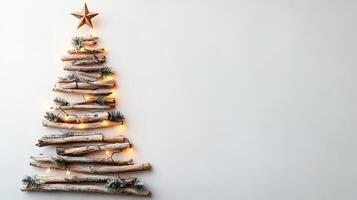 Christmas tree crafted from driftwood and adorned with lights and pinecones, set against a white wall. Christmas handmade decor and craftwork, eco friendly, sustainable concept. Place for text. photo