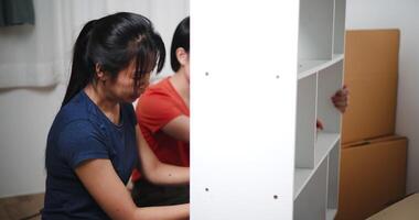 Handheld shot, Two siblings are happily chatting while assembling furniture together in the living room of their new house. Moving to a new home concept video
