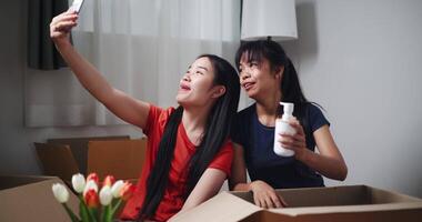 portátil tomada, dois irmãos sentar em a chão alegremente bate-papo por vídeo com amigos em Smartphone enquanto desembalar coisa a partir de caixas às Novo casa. comovente para uma Novo casa conceito video