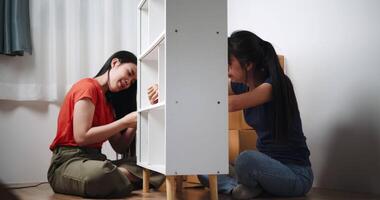 Handheld low angle view shot, Two siblings are happily chatting while assembling furniture together in the living room of their new house. Moving to a new home concept video