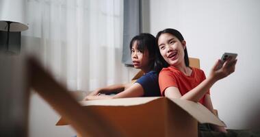 Handheld shot, Two young Asian women sit with backs to each other on the floor and discuss ideas for designing a room together in their new home. Moving to a new home concept video