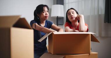 Handheld low angle view shot, Two Asian siblings sit on the floor talking as open boxes of items and exchange ideas on how to decorate different corners of new home. Moving and lifestyle concepts. video