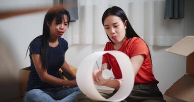Handheld selective focus shot, Two Asian women are helping to assemble a floor lamp in the living room in new home. Moving to a new home concept video
