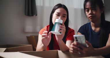 Handheld shot, Two siblings happily chatting on the floor and using mobile phone to check if the items in the boxes they moved from old house are complete. Moving to a new home concept video
