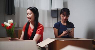 Handheld shot, Two siblings happily chatting on the floor and using mobile phone to check if the items in the boxes they moved from old house are complete. Moving to a new home concept video