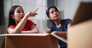 Handheld selective focus shot, Two Asian siblings sit on the floor talking as open boxes of items and exchange ideas on how to decorate different corners of new home. Moving and lifestyle concepts. video