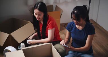 Handheld high angle view shot, Two siblings happily chatting on the floor and using mobile phone to check if the items in the boxes they moved from old house are complete. Moving to a new home concept video