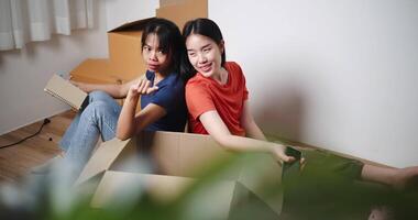 Handheld high angle view shot, Two young Asian women sit with backs to each other on the floor and discuss ideas for designing a room together in their new home. Moving to a new home concept video