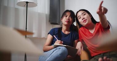 Handheld shot, Two Asian women are happily chatting and making a shopping list to decorate a room in new home. Moving to a new home concept video