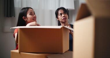 Handheld dolly shot, Two Asian siblings sit on the floor talking as open boxes of items and exchange ideas on how to decorate different corners of new home. Moving and lifestyle concepts. video
