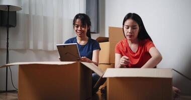 Handheld shot, Two Asian siblings sit on the floor, looking at a picture frame took out of a cardboard box, and laugh happily at new home. Moving to a new home concept video