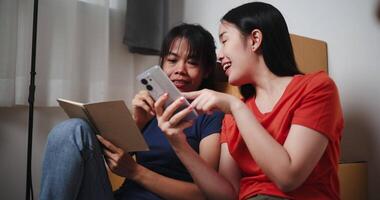 Handheld low angle view shot, Older sister is writing a shopping list in a notebook while the younger sister is shopping for household items via a mobile app. Moving to a new home concept video