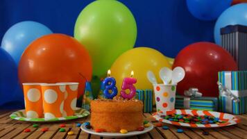 Birthday cake 35 on rustic wooden table with background of colorful balloons, gifts, plastic cups and plastic plate with candies and blue wall in the background photo