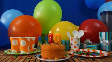 Birthday cake 10 on rustic wooden table with background of colorful balloons, gifts, plastic cups and plastic plate with candies and blue wall in the background photo