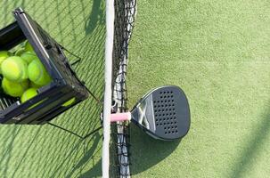 padel racket and yellow balls placed on court near net on sunny day photo