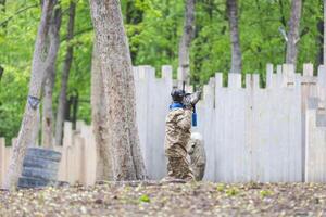 Paintball game. Players with weapons shooting paint balls. Men on the playground. Guys in camouflage and masks are fighting. photo