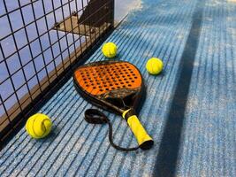 padel racket and yellow balls placed on court near net photo