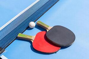 Red and black Table Tennis Paddles and ball on the blue table tennis table with net. Ping Pong concept with copy space photo