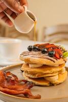 A breakfast of pancakes drizzled with honey, served with crispy bacon photo