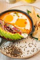 Breakfast with a casserole of sunny-side-up eggs, orange juice, fruits, and avocado photo