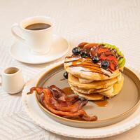 A breakfast of pancakes drizzled with honey, served with crispy bacon photo