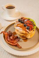 A breakfast of pancakes drizzled with honey, served with crispy bacon photo