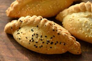 three empanadas with sesame seeds on a wooden cutting board photo