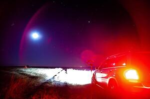 A car is parked in a field at night with a full moon behind it photo