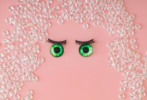 Surreal portrait made of diamonds, false green eyes and false eyelashes on pastel pink background. Minimal surreal concept. Flat lay style. photo