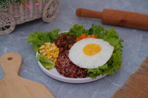 A vibrant meal consisting of red rice, meat, corn, carrots, lettuce, and a sunny side up egg photo