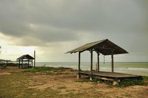 A wooden gazebo by a calm beach surrounded the sea beneath cloudy skies that creates a peaceful setting that embodies simplicity and solitude in the coastal landscape. photo