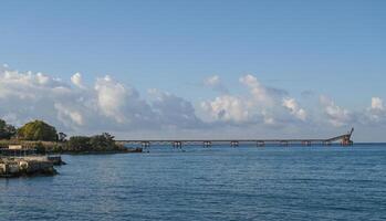 Vast blue waters meet a distant pier under a bright sky in a serene coastal landscape photo