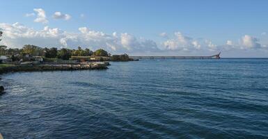 Serene coastal view with a distant pier under a clear blue sky during early afternoon light photo
