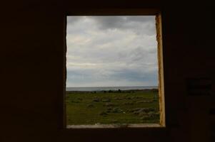 View through an open window showcasing a tranquil landscape by the sea under a moody sky photo
