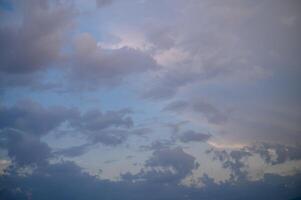 Dramatic clouds drift across a twilight sky, merging shades of blue and gray with hints of golden light photo