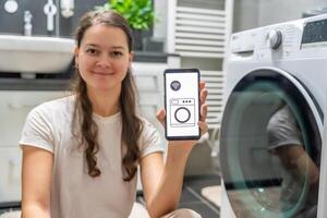 Young woman using mobile phone control via wi-fi and app for washing machine in home. Homesmart and new technology concept. High quality photo
