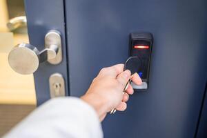 Close up view of person using a electric lock key fob to access a building via a reader of entry system mounted on a house wall. High quality photo