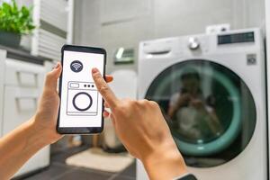 Young woman using mobile phone control via wi-fi and app for washing machine in home. Homesmart and new technology concept. High quality photo