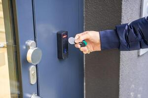 Close up view of person using a electric lock key fob to access a building via a reader of entry system mounted on a house wall. High quality photo
