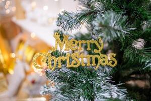 A close-up of a merry christmas text toy on a Christmas tree with lights on background. High quality photo