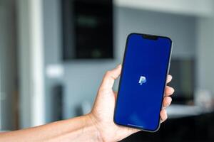 Prague, Czech republic - May 2, 2024. Woman holding iPhone with chat application PayPal on the screen, using mobile application for business home. High quality photo
