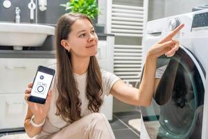 Young woman using mobile phone control via wi-fi and app for washing machine in home. Homesmart and new technology concept. High quality photo