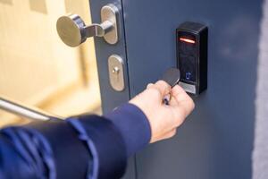 Close up view of person using a electric lock key fob to access a building via a reader of entry system mounted on a house wall. High quality photo