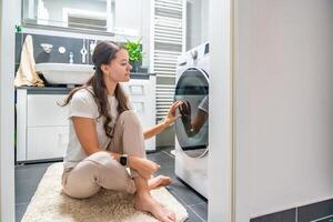 Young woman waiting for the washing machine to finish, looking at the washing machine door. High quality photo