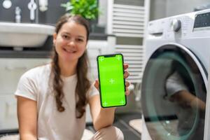 Young woman using mobile phone control via wi-fi and app for washing machine in home. Homesmart app, chroma key green screen. High quality photo